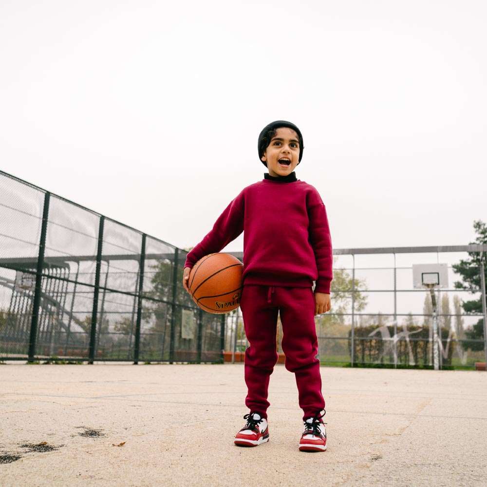 Children Urban Basic Jogginghose - Bordeaux Kind mit Ball am Basketballplatz